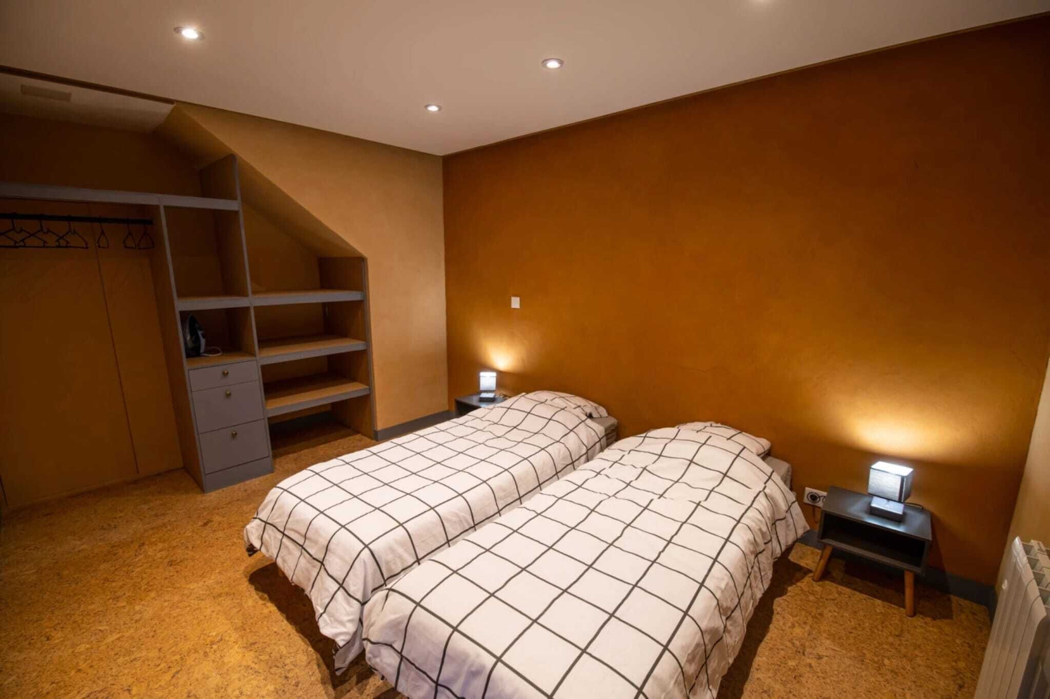 A bedroom with two beds, a wardrobe, and a small desk with a lamp.