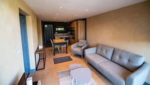 Una sala de estar moderna con un sofá gris, una mesa de comedor con sillas y una cocina al fondo.