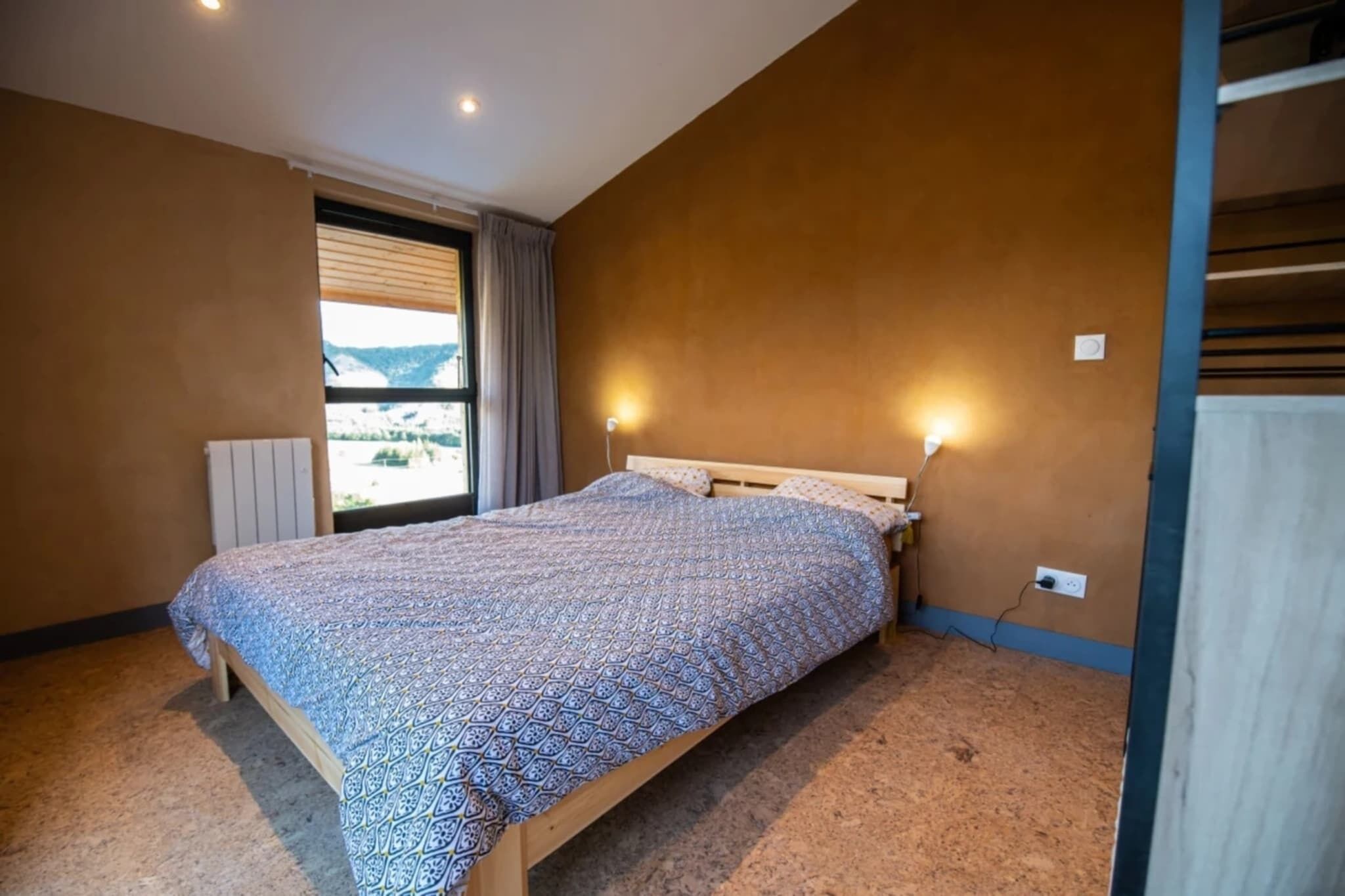 Een slaapkamer met een bed, een raam met gordijnen en een wandlamp.