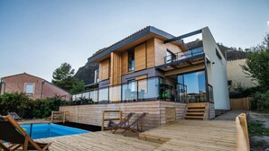 Una casa moderna con terraza de madera, piscina y balcón.