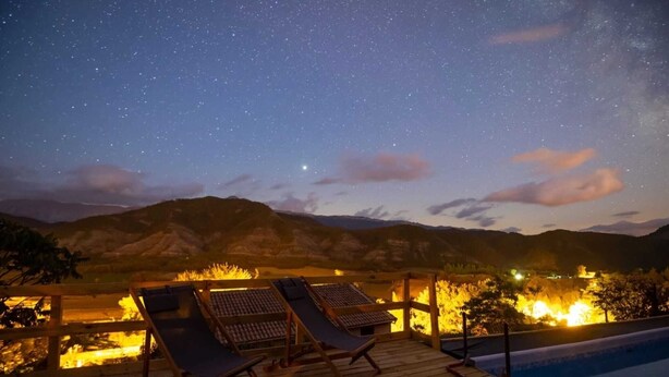 Terraza de madera con sillones de descanso con vistas a una piscina y un cielo nocturno lleno de estrellas.