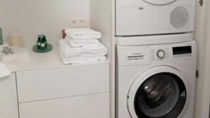 A compact laundry area with stacked washing machines and a small countertop with folded towels. - Suite aux Anges N°1 (Antwerpen)