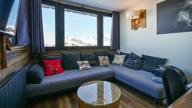 A modern living room with a sectional sofa, a round coffee table, and a large window with a mountain view. - Apartment “Lesetoilesdelaplagne - Le Diamant” with Mountain View and Private Terrace (aime la plagne)