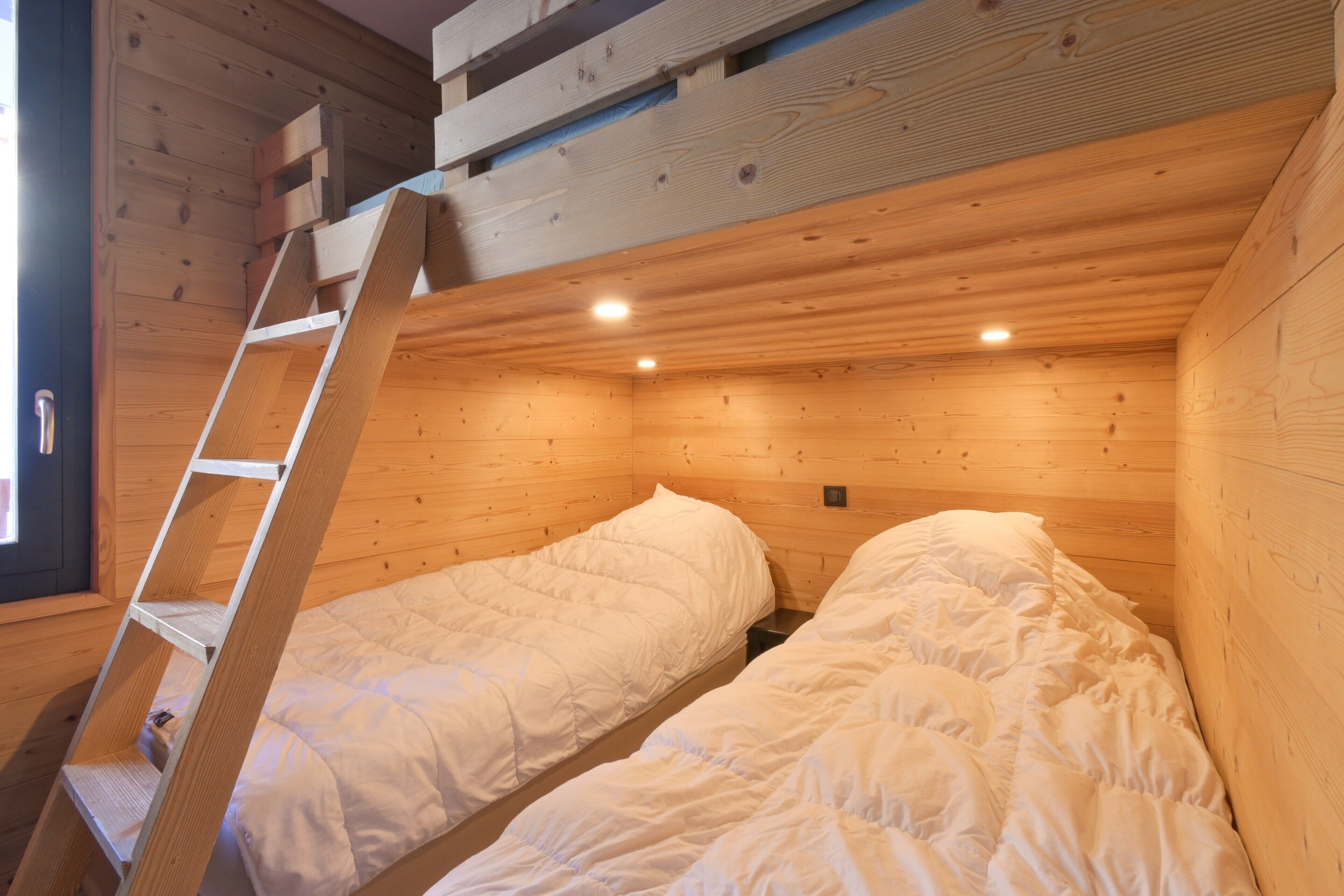 Una cabaña de madera con dos literas, una escalera y un ventanal pequeño.