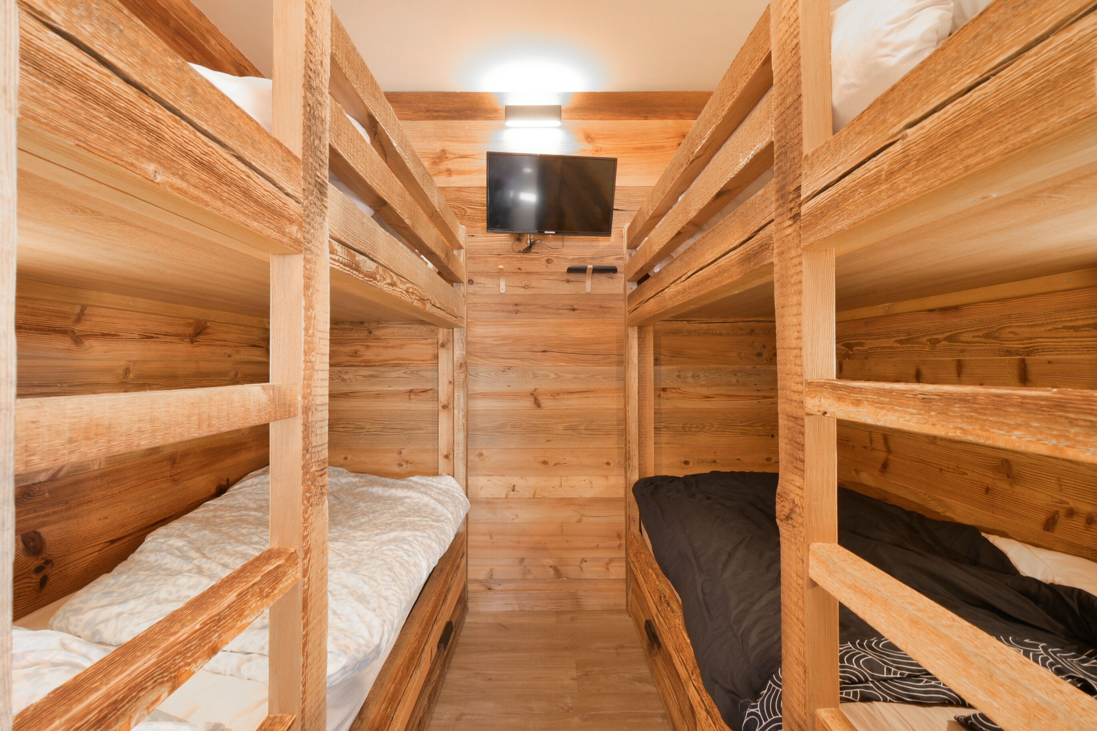 Une chambre avec des lits superposés, des murs en bois, un téléviseur fixé au mur et un luminaire au plafond.