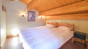 A bedroom with a wooden ceiling, a bed with white bedding, a nightstand, and a wall-mounted light fixture. - Spacious Chalet-Style Triplex Apartment for 10 in Belle Plagne, Ski-In/Ski-Out (La Plagne Tarentaise)