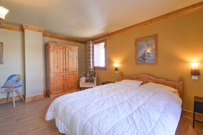 A bedroom with a large bed, wooden wardrobe, chair, and a painting on the wall.