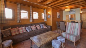 A wooden interior with a sofa, chairs, a table, and a kitchen area.