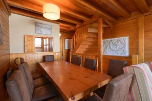 A wooden interior with a dining table, chairs, a staircase, and a map on the wall.