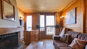 Interior acolhedor de uma cabana com lareira, paredes de madeira, um sofá e um quadro.