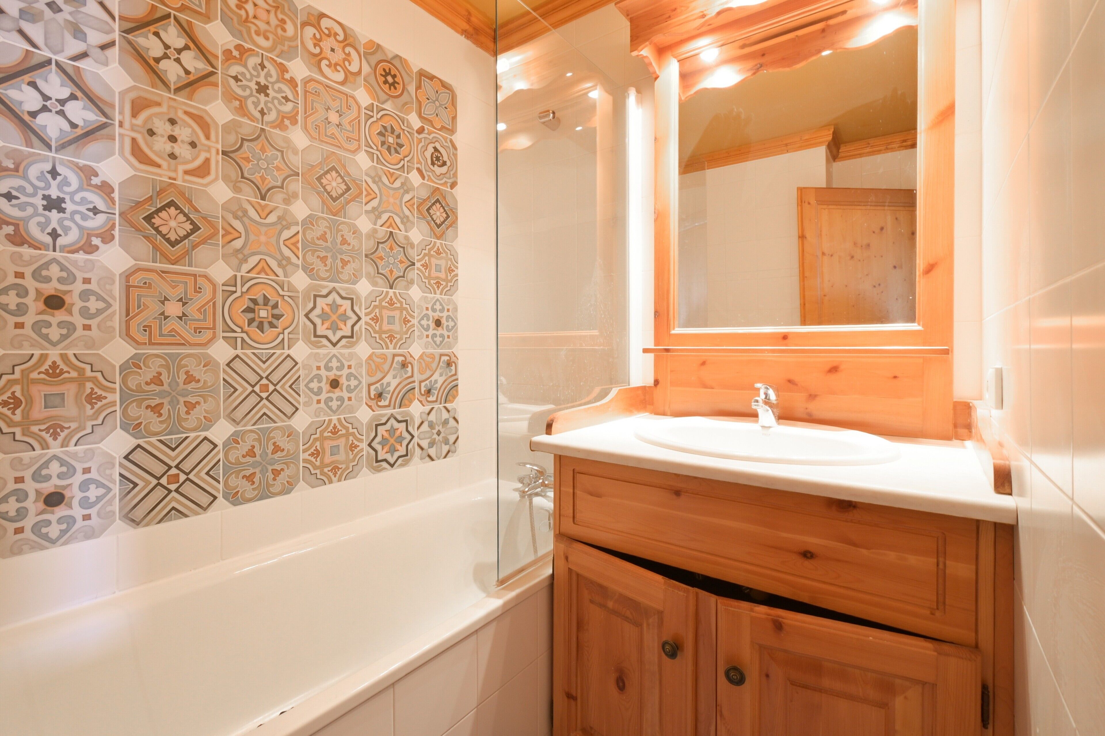 Une salle de bain avec un mur carrelé, une baignoire, un meuble-lavabo en bois et un miroir.