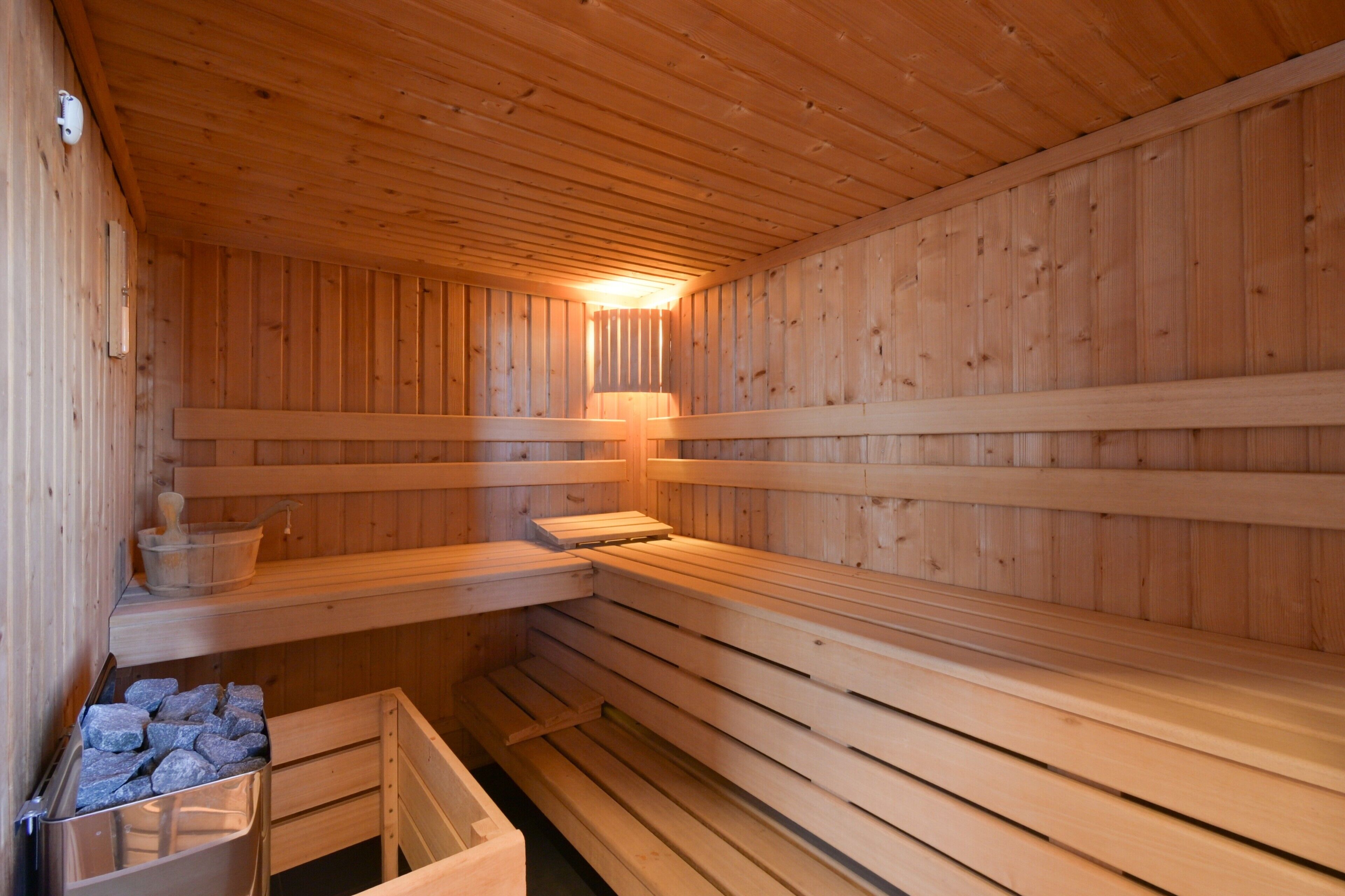Un sauna avec des bancs en bois, un réchauffeur de banc et un seau rempli de pierres.