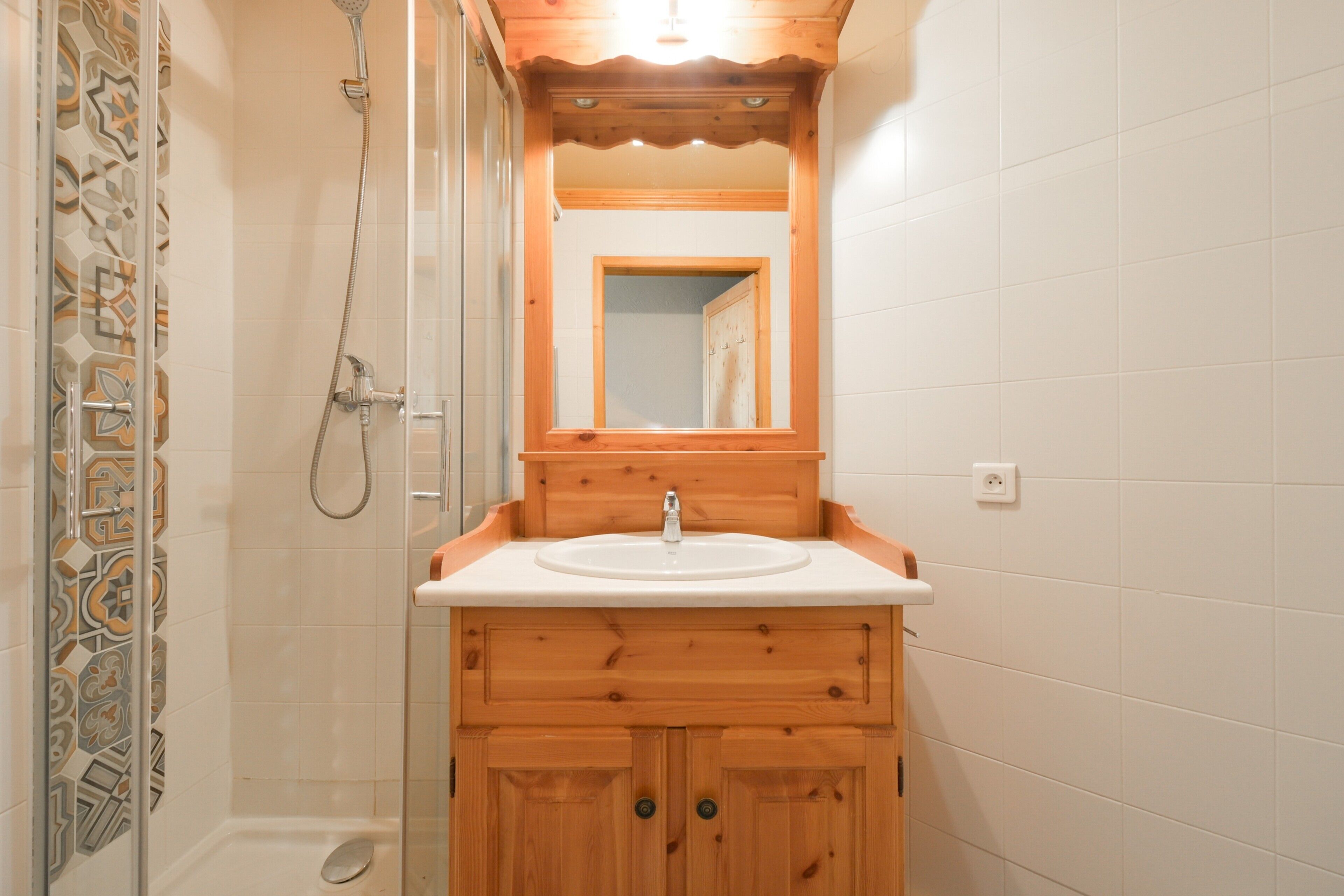 A bathroom with a wooden vanity, a sink, a mirror, and a shower.