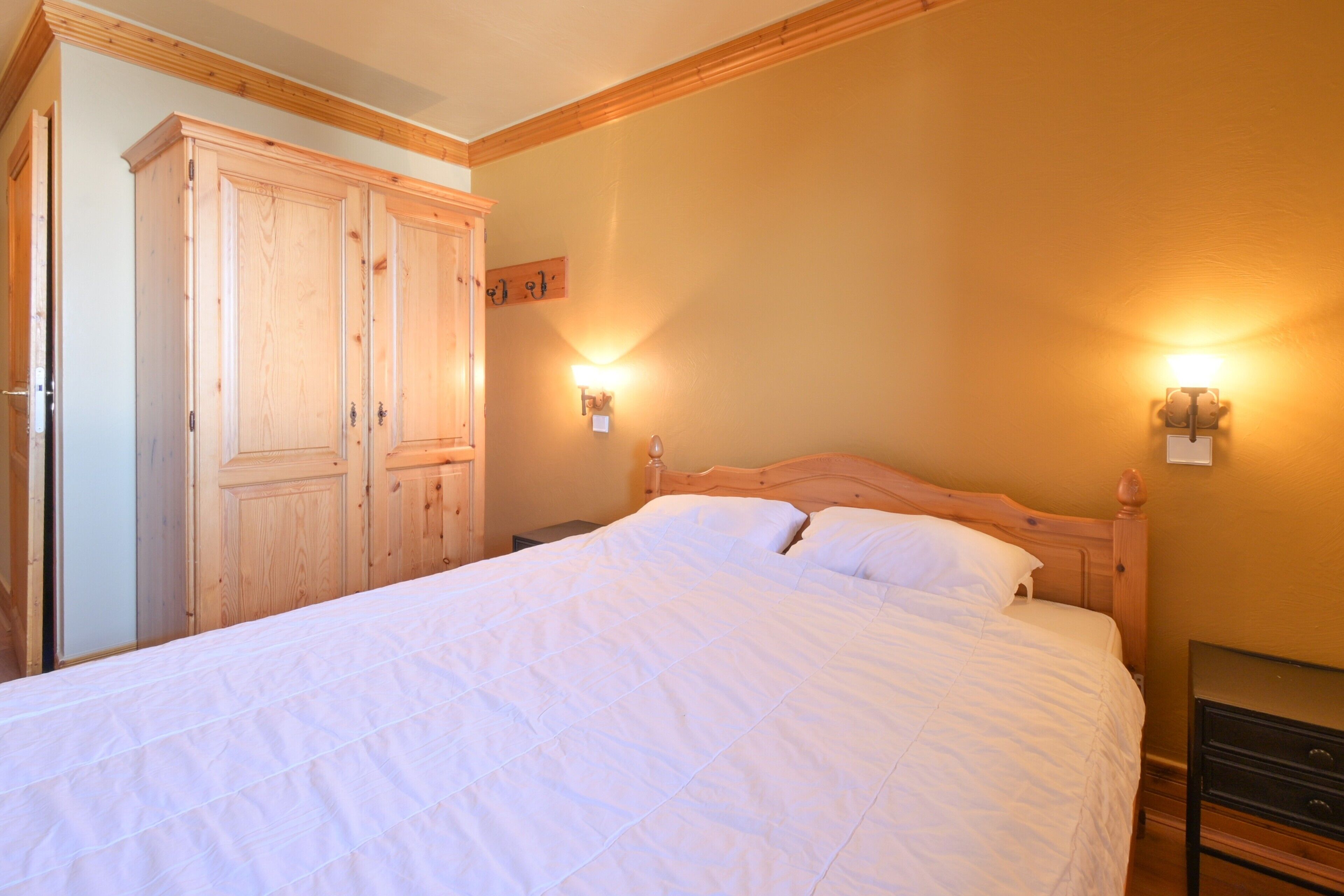 A bedroom with a wooden bed, two wall-mounted lights, and a wardrobe.