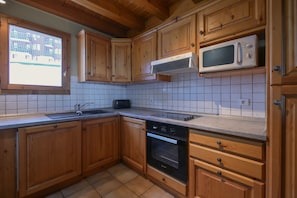 Una cocina con armarios de madera, microondas, lavavajillas y ventana con vista a edificios.