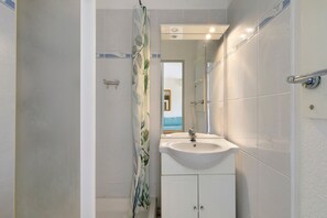 A bathroom with a white sink, a mirror, and a shower curtain with a leaf pattern. - Apartment 'Cap d’Agde - Primavera - 1' with Shared Pool, Private Terrace and Air Conditioning (Agde)