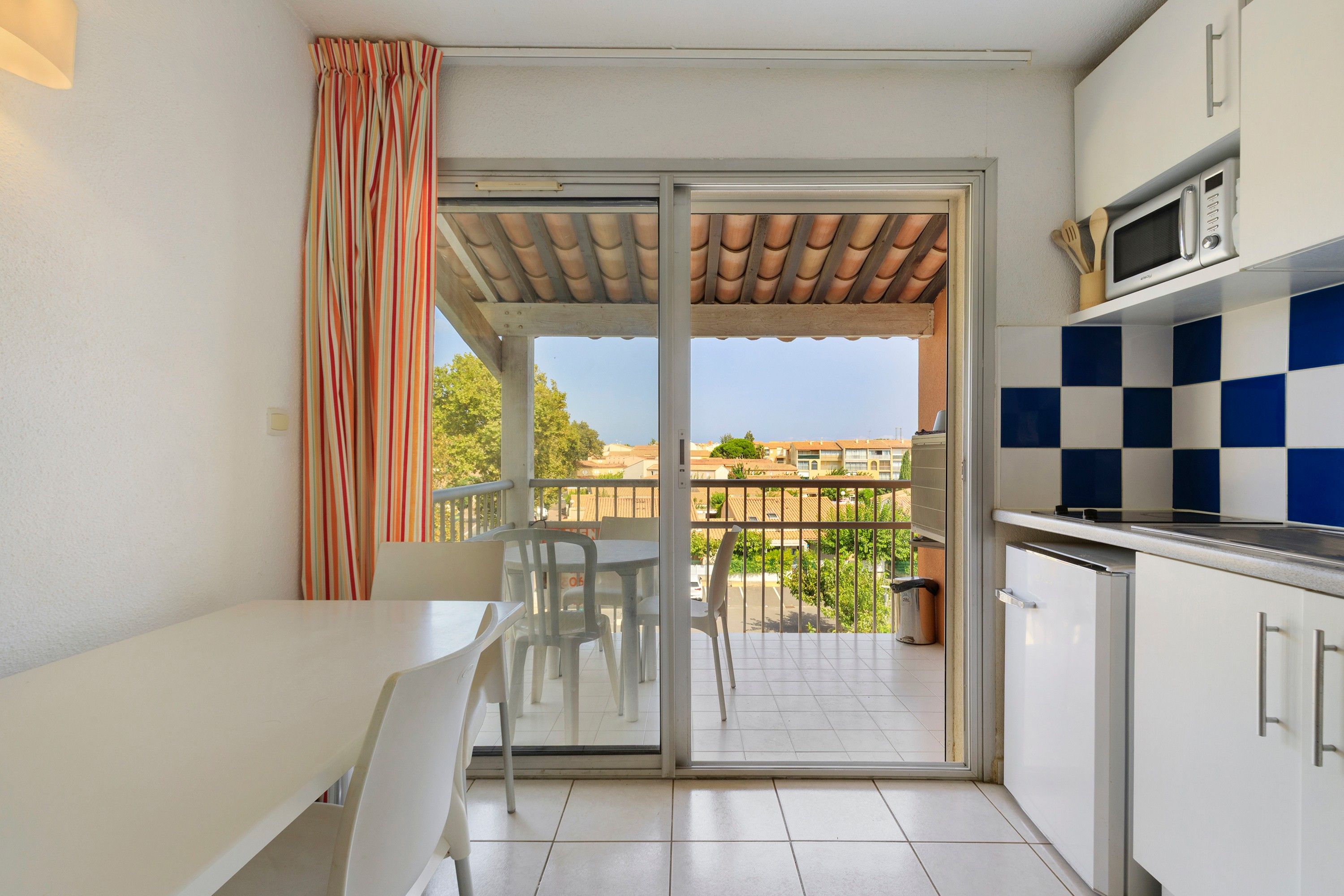A small kitchen with a microwave, a tiled backsplash, and a sliding glass door leading to a balcony with outdoor furniture.