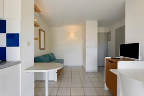 Ett kompakt bostadsutrymme med ett litet kök, ett litet matbord, en soffa och en TV.