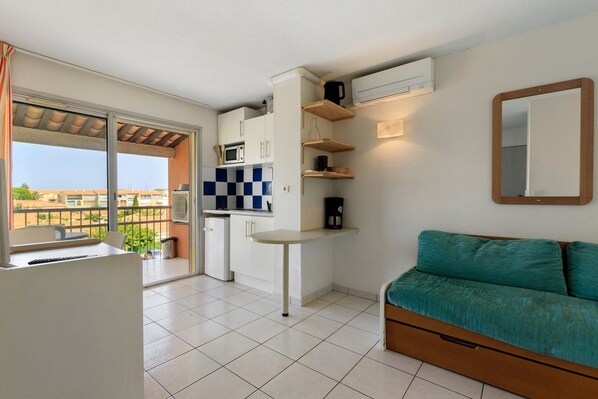 A compact living space with a kitchenette, a dining area, and a sofa. - Apartment 'Cap d’Agde - Primavera - 1' with Shared Pool, Private Terrace and Air Conditioning (Agde)