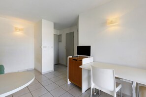 Ett hotellrum med ett vitt skrivbord, en stol, en tv-apparat placerad på ett träskåp och en dörr som leder till ett annat rum.