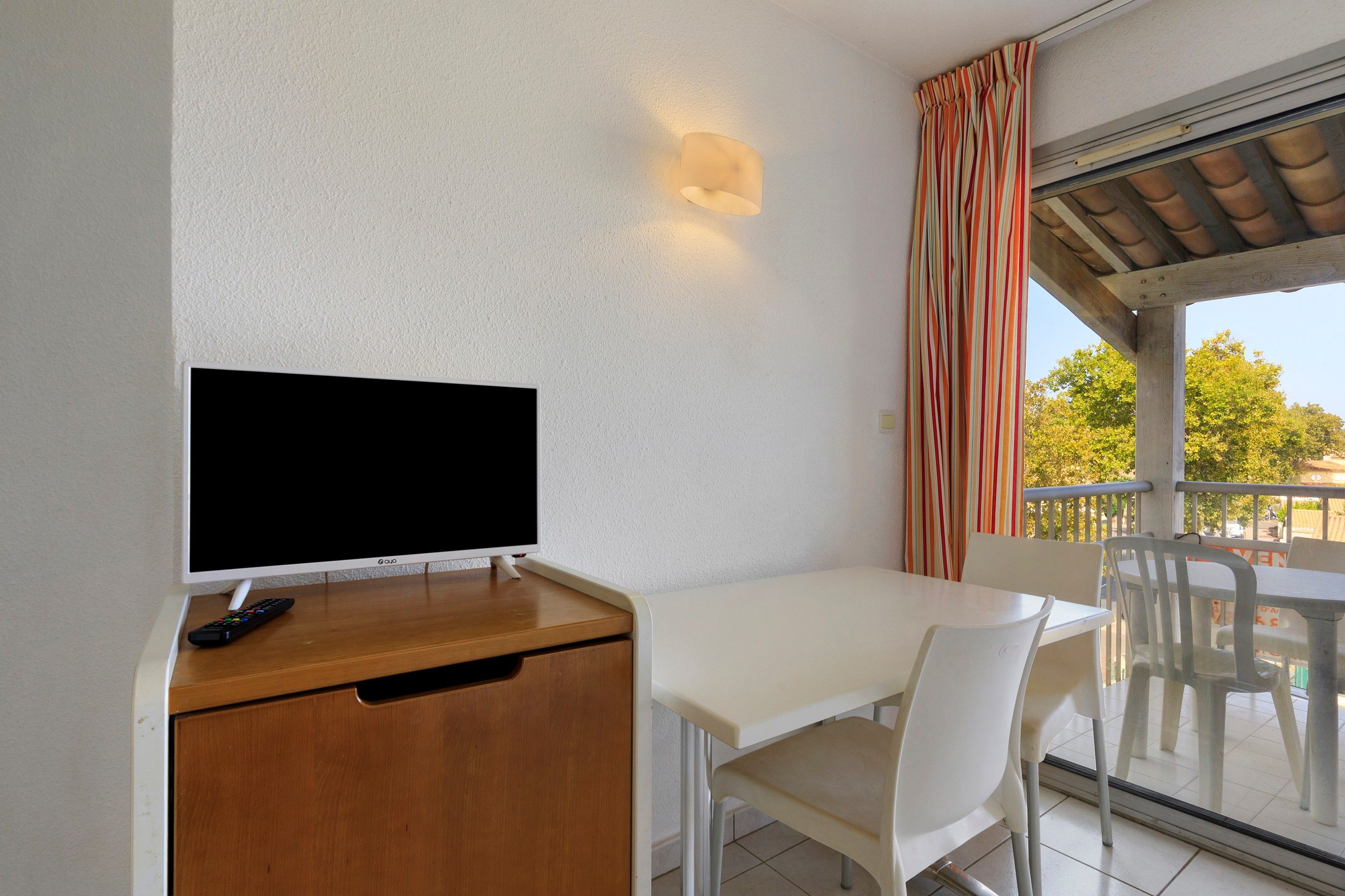 A room with a television on a wooden cabinet, a white table, and chairs.