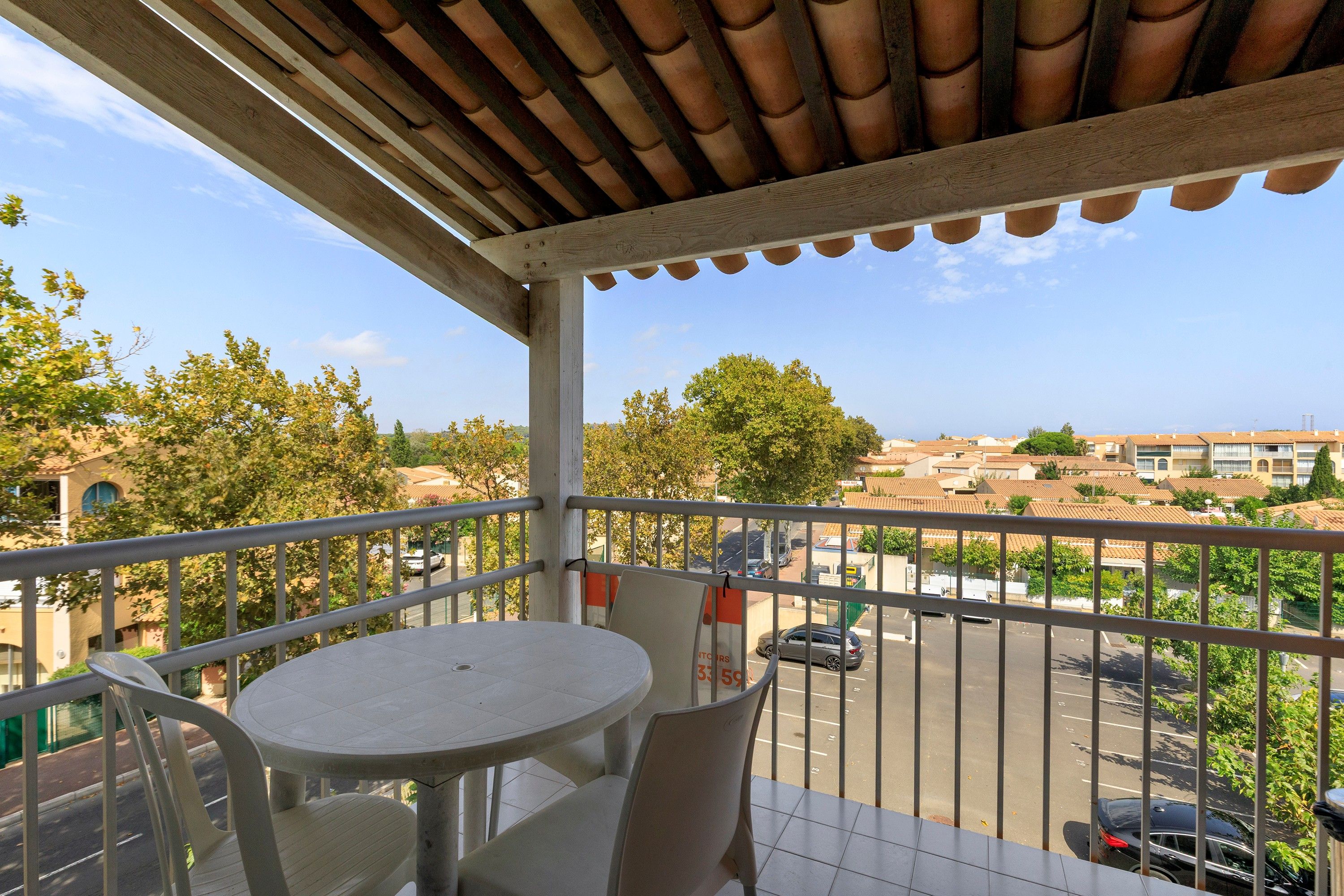 A balcony with a table and chairs, overlooking a street with parked cars and buildings.