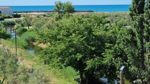 A coastal landscape with a clear view of the sea, a small body of water, and dense greenery. - Apartment 'Cap d'Agde - Primavera - 2' with Sea View, Shared Pool and Air Conditioning (Agde)