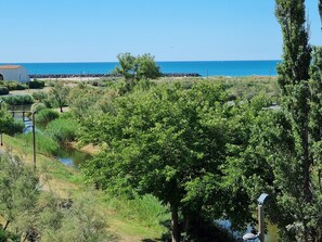 A coastal landscape with a clear view of the sea, a small body of water, and dense greenery. - Apartment 'Cap d'Agde - Primavera - 2' with Sea View, Shared Pool and Air Conditioning (Agde)