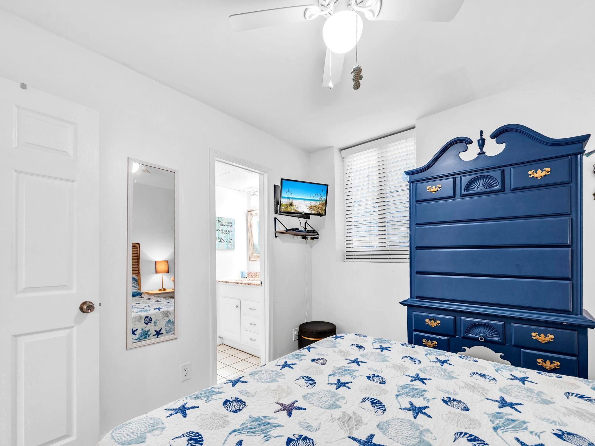 Une chambre à coucher comprenant un lit, une commode, un téléviseur et une fenêtre avec des stores.