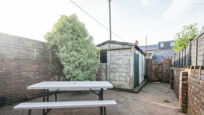 Ein Picknicktisch in einem Garten mit einer Ziegelmauer, einem kleinen Schuppen und einem Baum.
