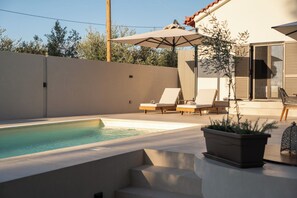 A modern outdoor pool area with lounge chairs and a large umbrella. - Amazing waterfront villa with pool and Ionian sea sunsets direct access to beach (Nestor)