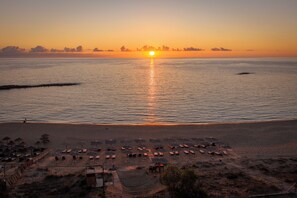 A beach with sun loungers and umbrellas, a clear sky, and the sun setting over the water. - Amazing waterfront villa with pool and Ionian sea sunsets direct access to beach (Nestor)