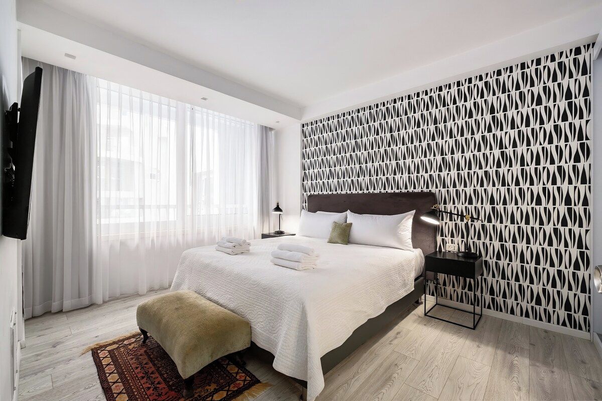 Une chambre d’hôtel moderne avec un grand lit, une table de chevet, une lampe et un panneau décoratif au mur.