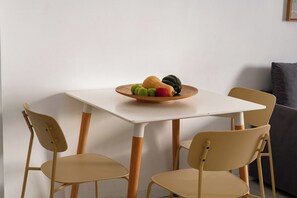 Ein Essbereich mit einem weißen Tisch, vier beigen Stühlen und einer Obstschale auf dem Tisch.