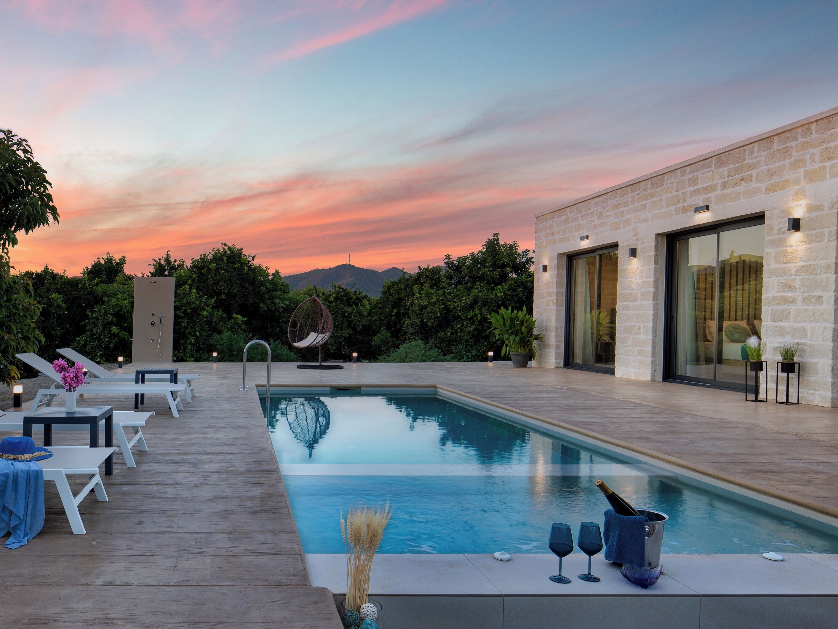 A modern outdoor pool area with lounge chairs, a hot tub, and a bottle of champagne.