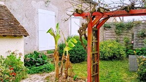 Ein Garten mit rotem Spalier, einem gepflasterten Weg und einem Haus mit weißer Tür und Ziegeldach.
