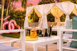An outdoor patio area with a white table set for drinks, a canopy, and a wicker sofa. - Designer 4BR Villa • Pool • 30 min to WC Stadium (Fort Lauderdale)