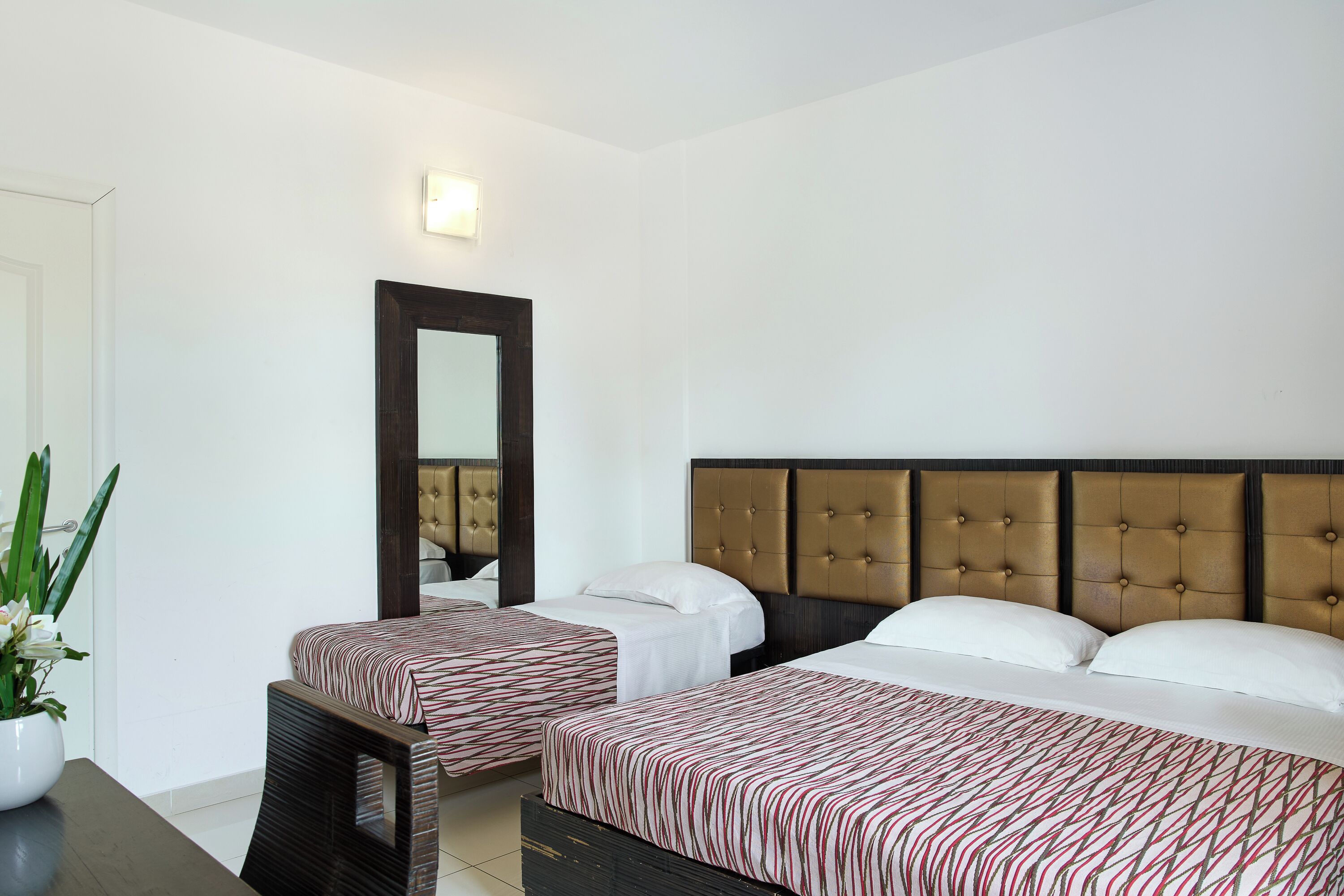 Camera d'albergo con due letti, un ampio specchio, una pianta in vaso e un comodino.