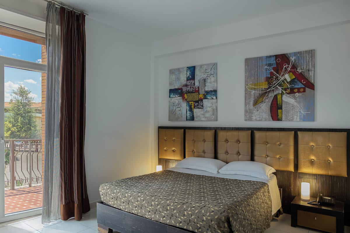 A bedroom with a large bed, a nightstand, and two abstract paintings on the wall.