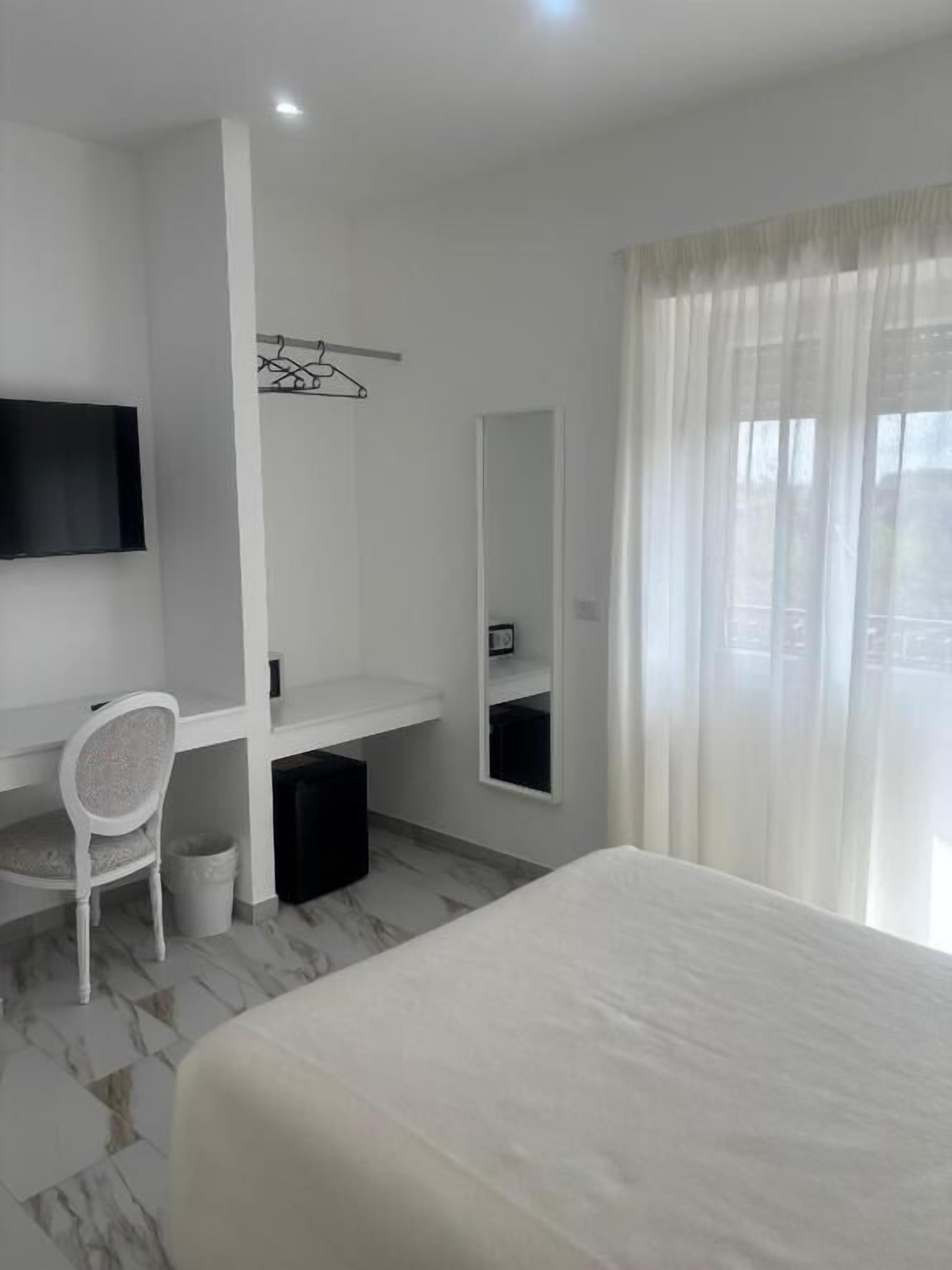 A hotel room with a bed, a desk, a chair, a television, a mirror, and a window with curtains.