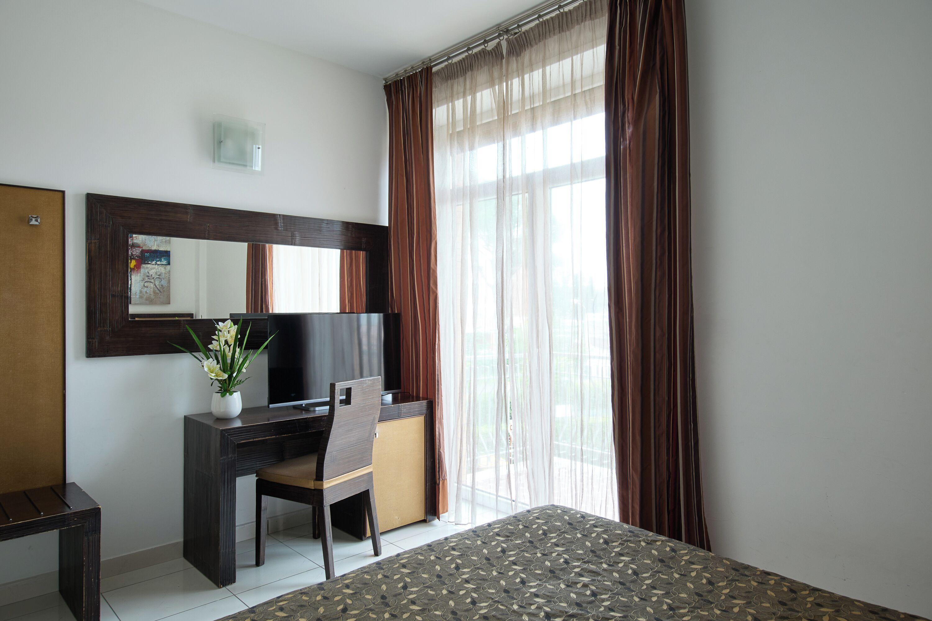 A hotel room with a bed, a desk, a chair, a television, and a window with curtains.