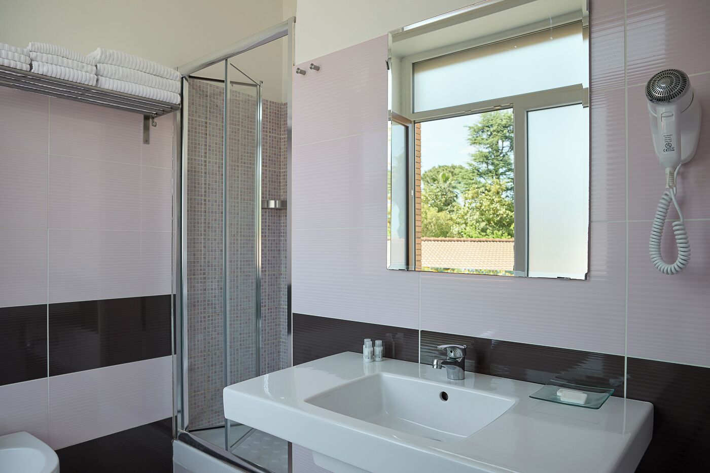 A modern bathroom with a glass shower enclosure, a white sink, and a hairdryer mounted on the wall.