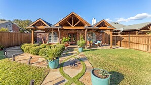 A two-story house with a covered patio, stone pathway, and potted plants. - Luxury Pool Home w/ Outdoor Lounge Near Stadium (Irving)