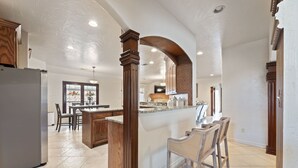 A spacious kitchen with a central island, wooden cabinetry, and a large window. - Luxury Pool Home w/ Outdoor Lounge Near Stadium (Irving)