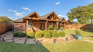 A two-story brick house with a wooden deck and a fenced backyard. - Luxury Pool Home w/ Outdoor Lounge Near Stadium (Irving)
