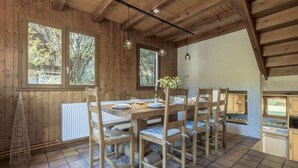 Un comedor de madera con una mesa grande y sillas, un radiador blanco y vistas a árboles a través de las ventanas.