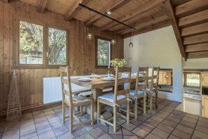 A wooden dining room with a large table and chairs, a white radiator, and a view of trees through the windows. - Chalet Cusco Spacious 4 Bed Traditional Chalet Servoz (Servoz)