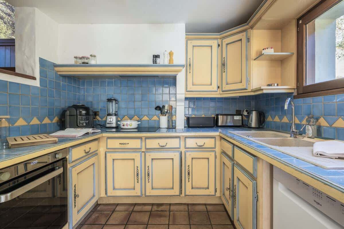 Una cocina compacta con salpicadero de azulejos azules, armarios amarillos y electrodomésticos básicos.