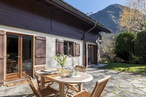 Uma casa de madeira com um pátio de pedra, móveis de madeira e um vaso com planta.