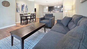 Ein modernes Wohnzimmer mit einem grauen Sofa, einem Holztisch und einem Essbereich mit einem dunklen Holztisch und Stühlen.